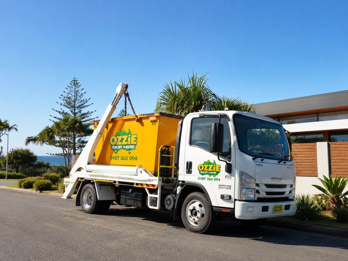 Ozzie Skip Hire truck delivering a yellow skip bin to a coastal home